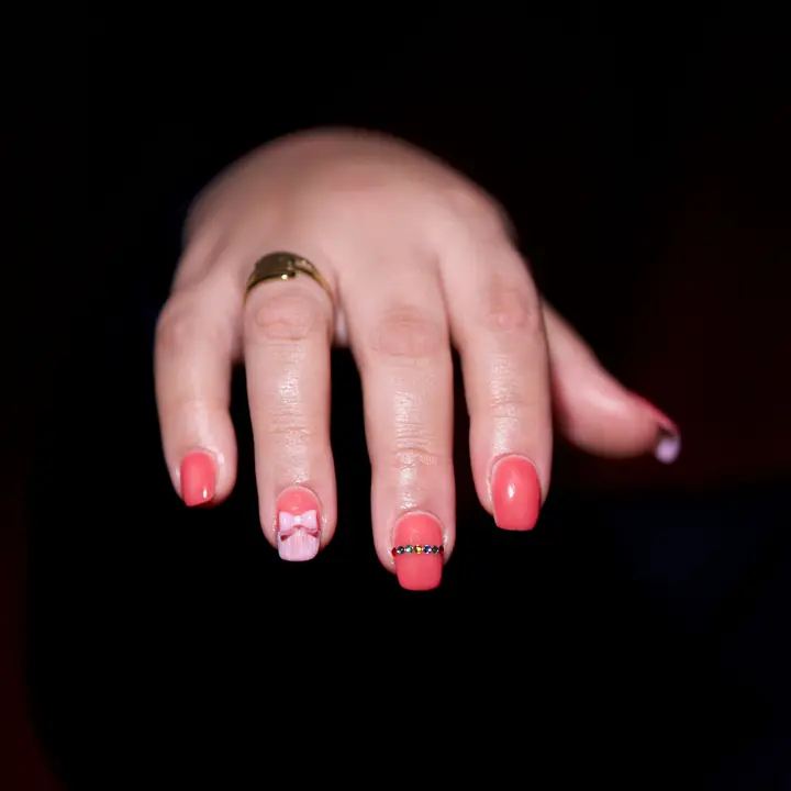 Pink nail art with a gold ring on a dark background